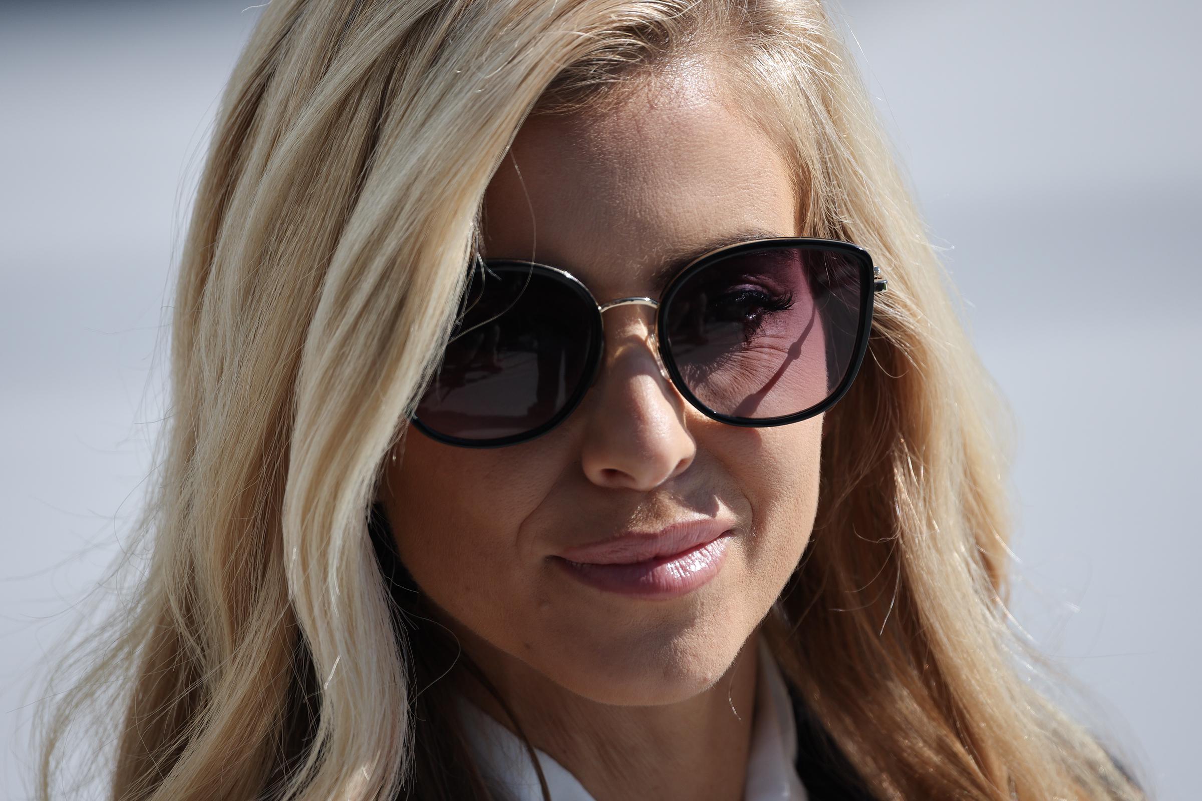 White House Press Secretary Katie Zacharia looks on from the South Lawn of the White House on October 13, 2026, in Washington, D.C. She wears oversized black-rimmed sunglasses with tinted gradient lenses and a white collared blouse, her blonde hair falling in soft waves around her face as she stands listening outdoors. | Source: Getty Images
