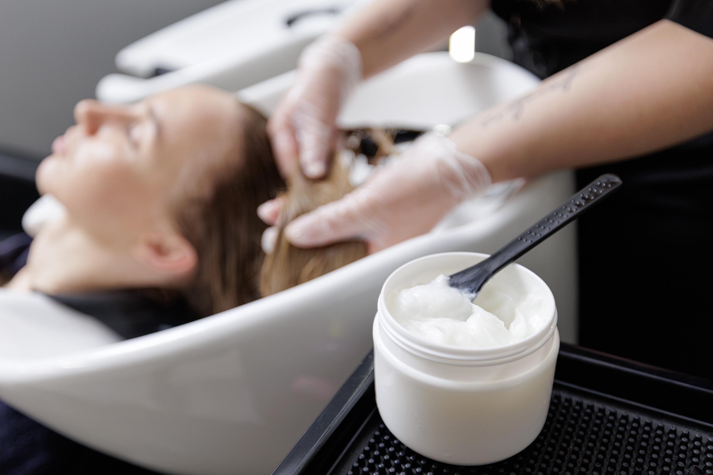 A stylist applies a nourishing hair mask to a woman's hair | Source: Getty Images