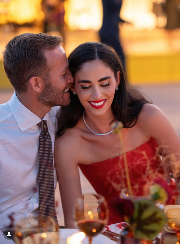 Juliette Dell beams with a bright red lip while wearing a strapless red dress and delicate diamond necklace as husband Chase Chamberlin leans in close with an affectionate smile during an outdoor celebration. | Source: Instagram/juliette_dell