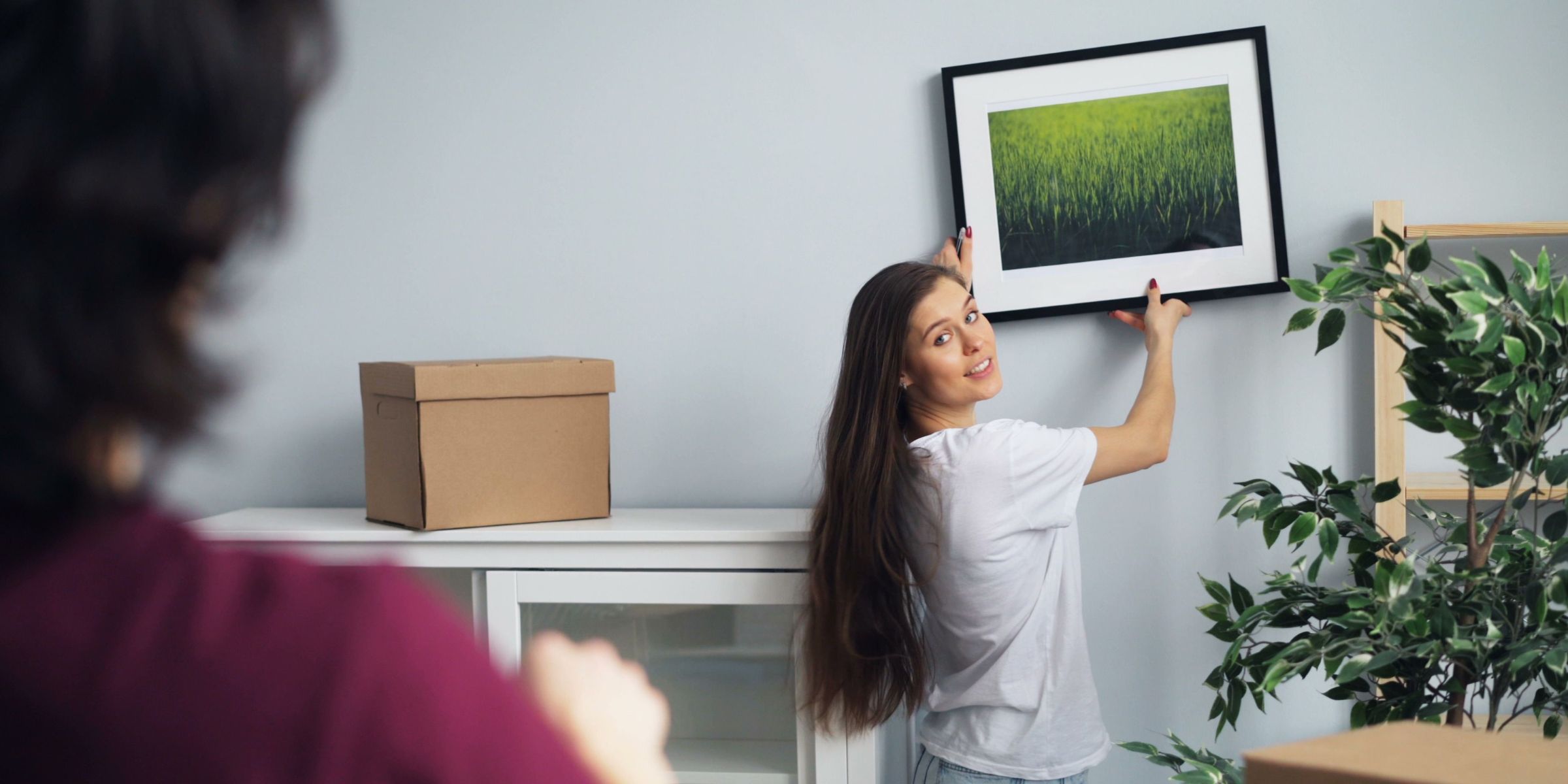 A woman hangs a framed picture on a wall while another person watches | Source: Pexels