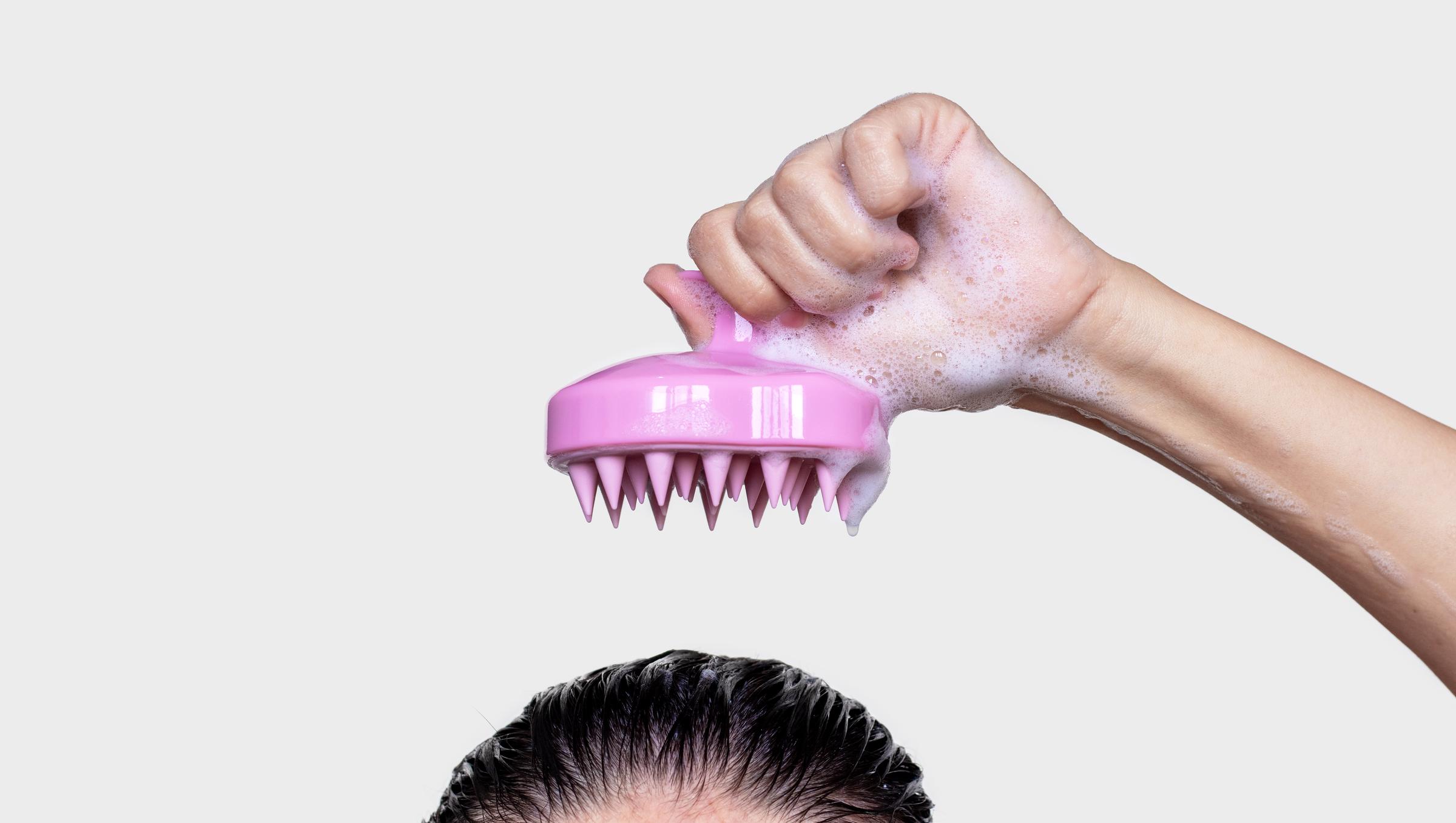 A woman using silicone pink shampoo brush for scalp massage hair growth stimulation | Source: Getty Images