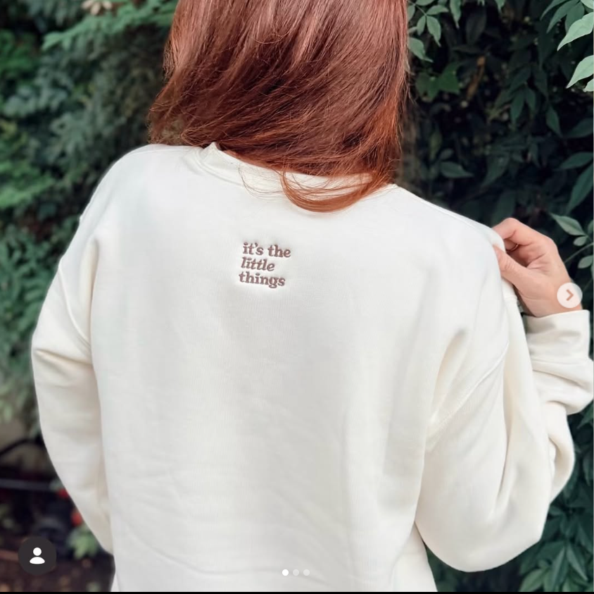 The cream-colored sweatshirt features “It’s the Little Things” embroidered in brown across the upper back. | Source: Instagram/momsofferingmore