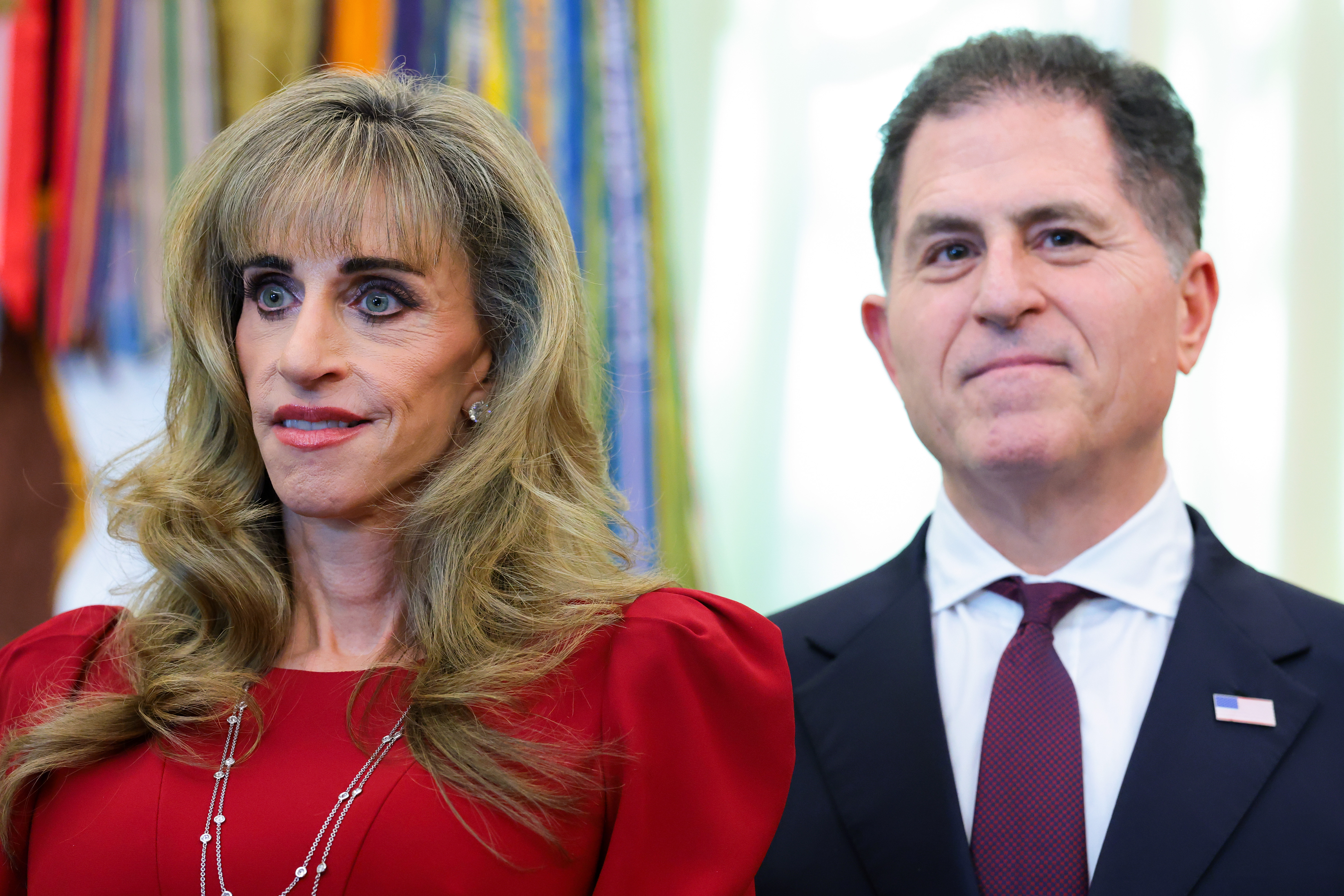 Dell Technologies CEO Michael Dell and his wife, Susan Dell, look on during an event in the Oval Office at the White House on October 7, 2026, in Washington, D.C. Susan wears an elegant red dress featuring subtle puff sleeves and layered delicate necklaces, standing beside Michael in a dark tailored suit, white collared shirt, and maroon necktie as President Donald Trump announced the activation of automatic enrollment for the "Trump Accounts" seed deposit program. | Source: Getty Images