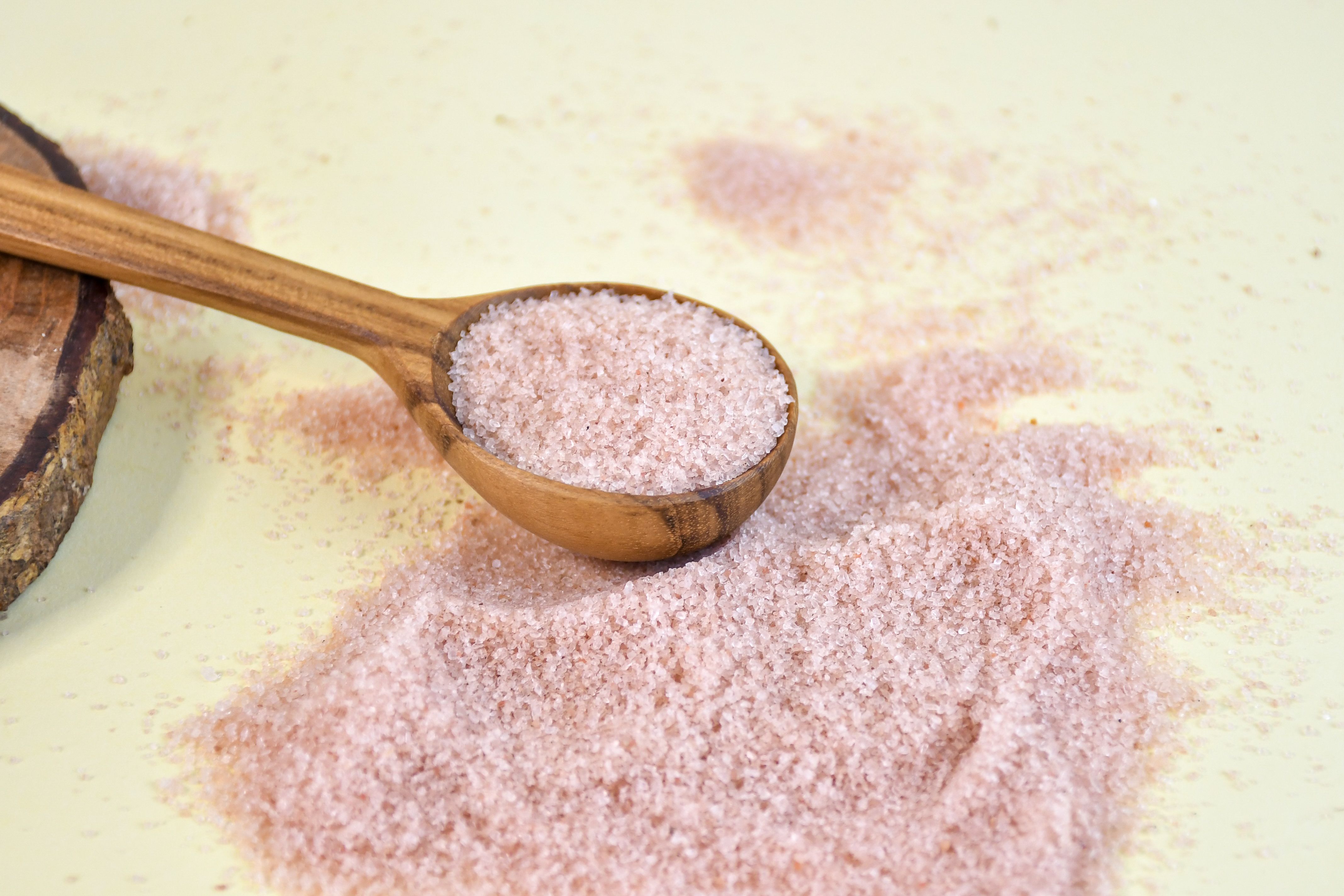 Crushed pink Himalayan salt displayed in a wooden spoon and on a table | Source: Pexels