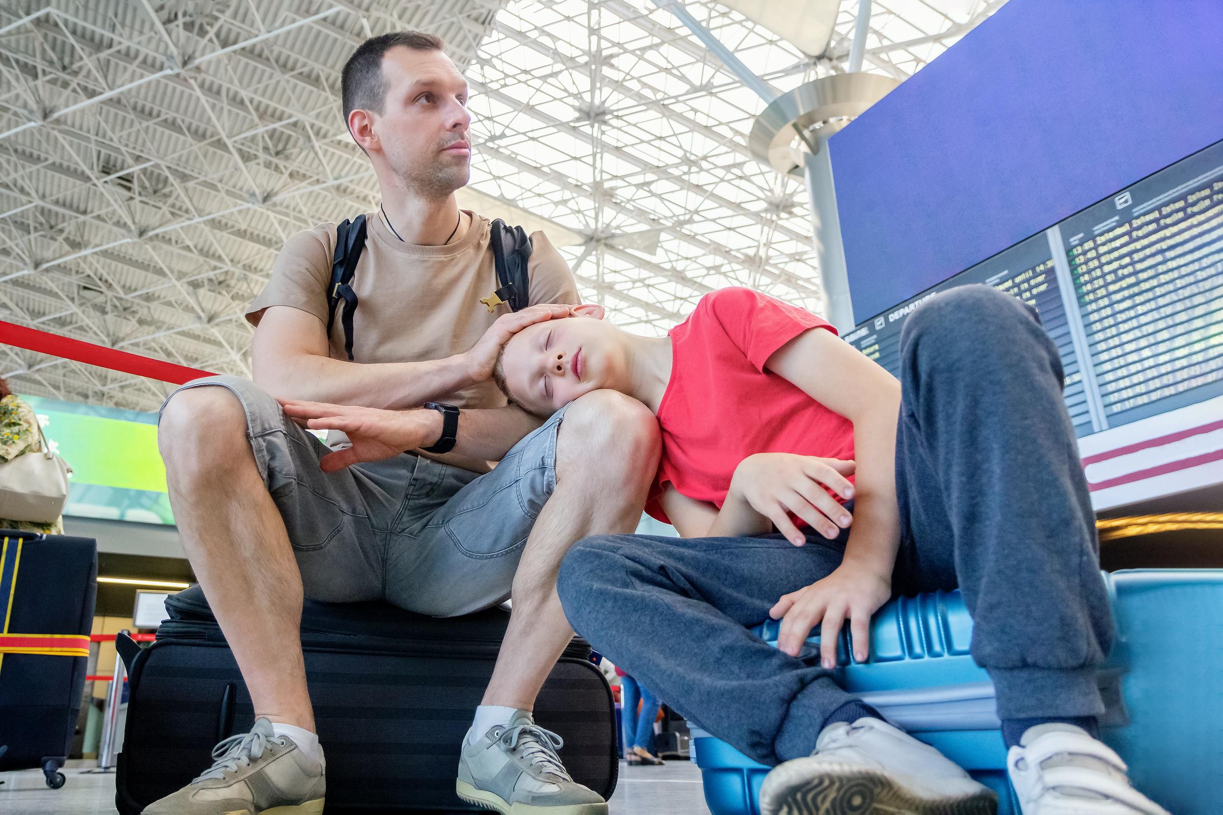 A tired child sleeping on his father's lap while sitting on suitcases at the departure board | Source: Getty Images