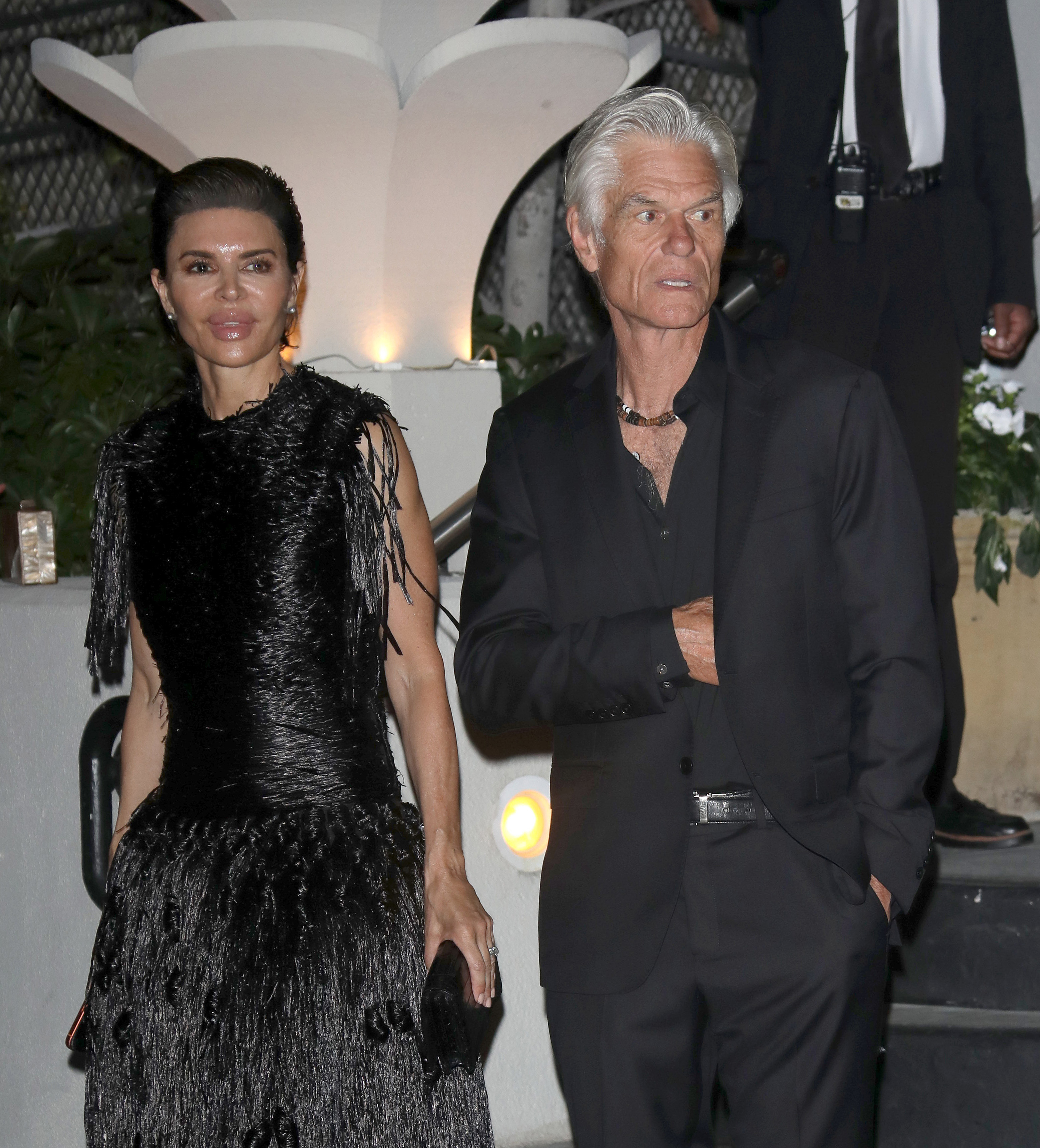 Lisa Rinna and Harry Hamlin pose together at The Hollywood Reporter x SAG-AFTRA Emmy Nominees Night, with Rinna's textured black gown and cascading fringe contrasting with Hamlin's sleek all-black suit and layered necklace. | Source: Getty Images