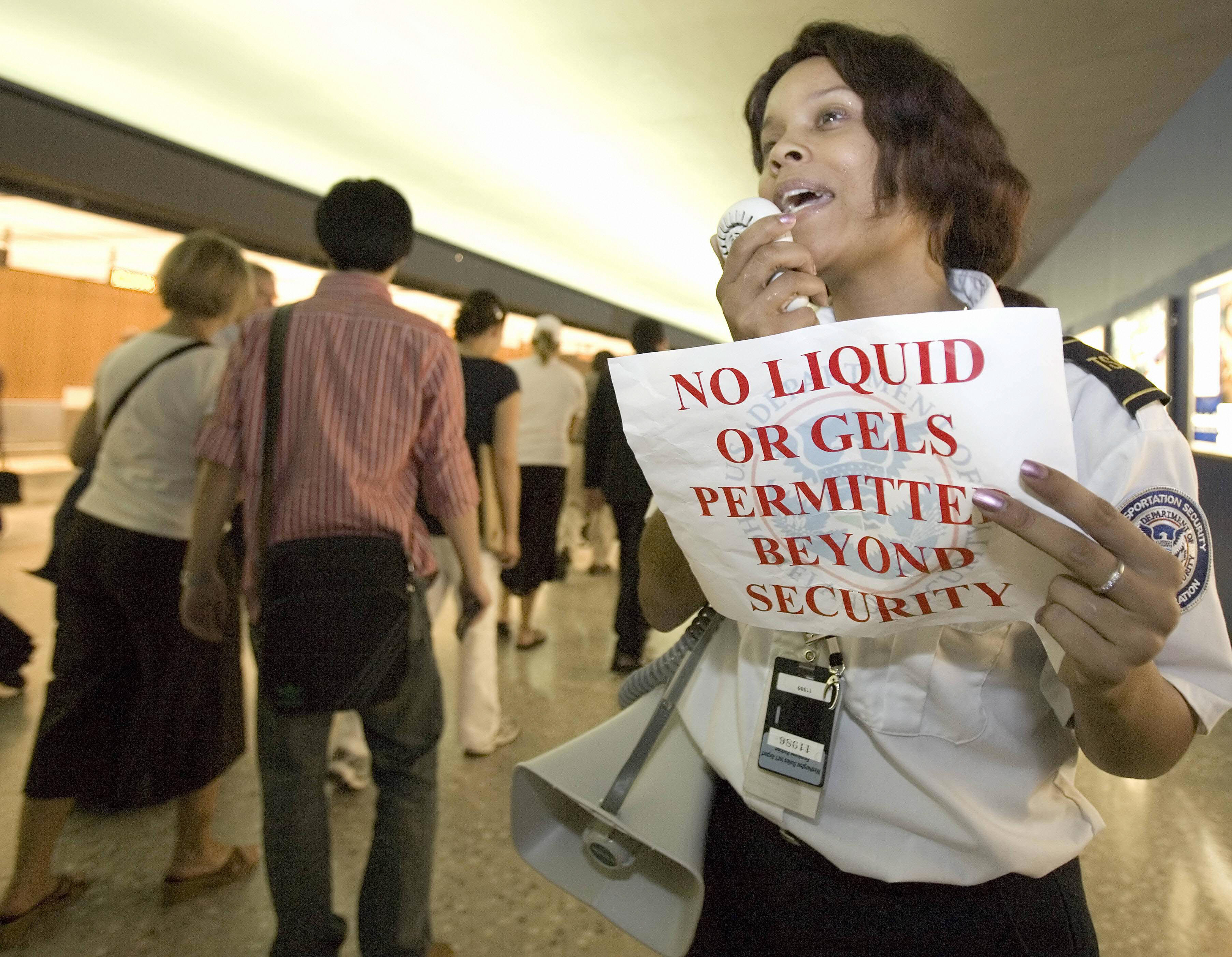 An airport security officer holds up a sign as she speaks on a bullhorn warning passengers about the rule on liquids and gels | Source: Getty Images