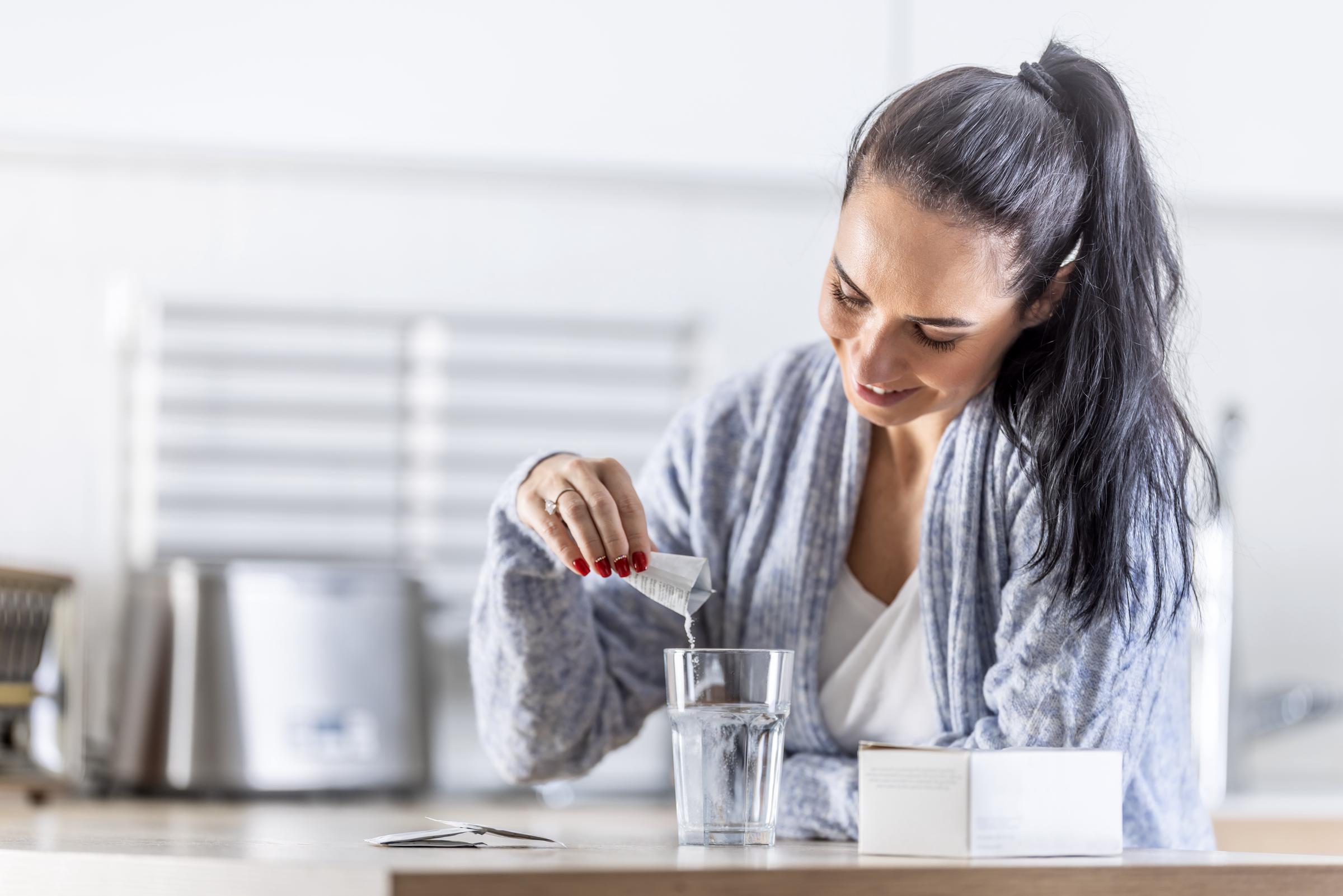 A young woman pours magnesium powder into a glass of water | Source: Getty Images