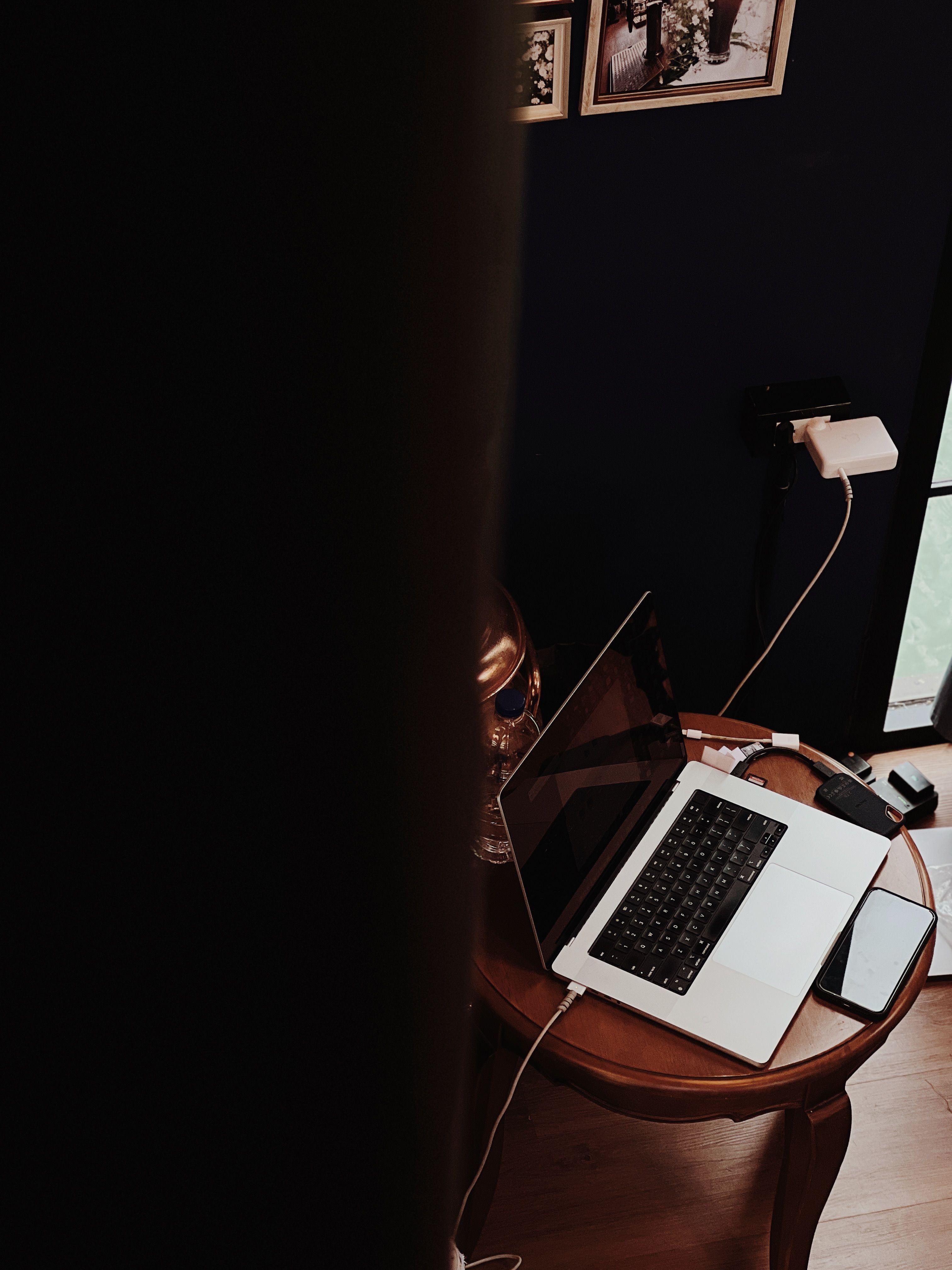 A laptop and a phone sit on a small round table, with a charger plugged into a wall outlet. | Source: Pexels