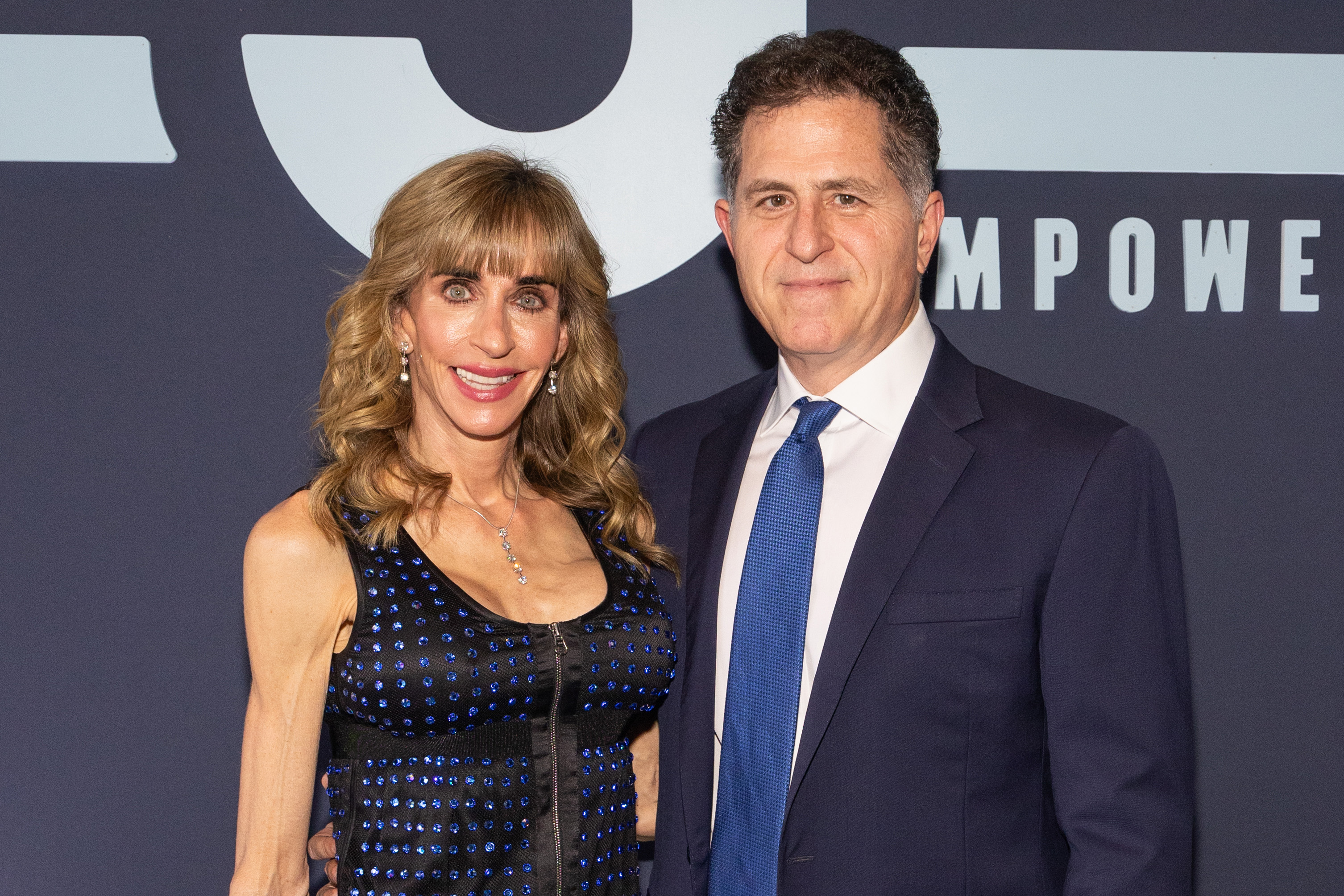 Susan Dell and Michael Dell smiled side by side while attending the 12th Annual Mack, Jack & McConaughey Gala at ACL Live on April 25, 2024, in Austin, Texas. Susan wore a black sleeveless dress adorned with blue rhinestones and a center front zipper, accessorized with drop earrings and a pendant necklace, while Michael stood beside her in a classic dark navy suit, white shirt, and royal blue tie. | Source: Getty Images