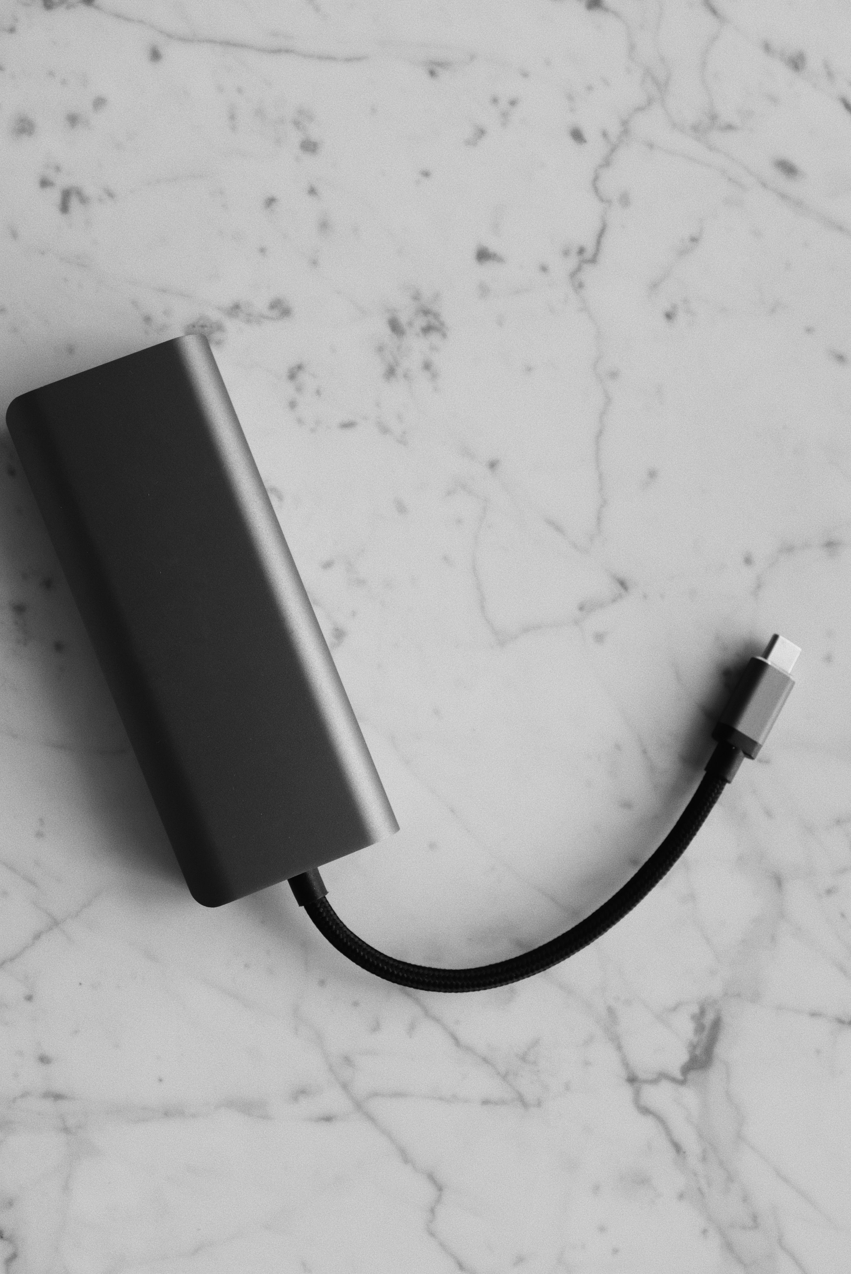 A gray power bank with a short braided cable lies on a marble surface. | Source: Pexels