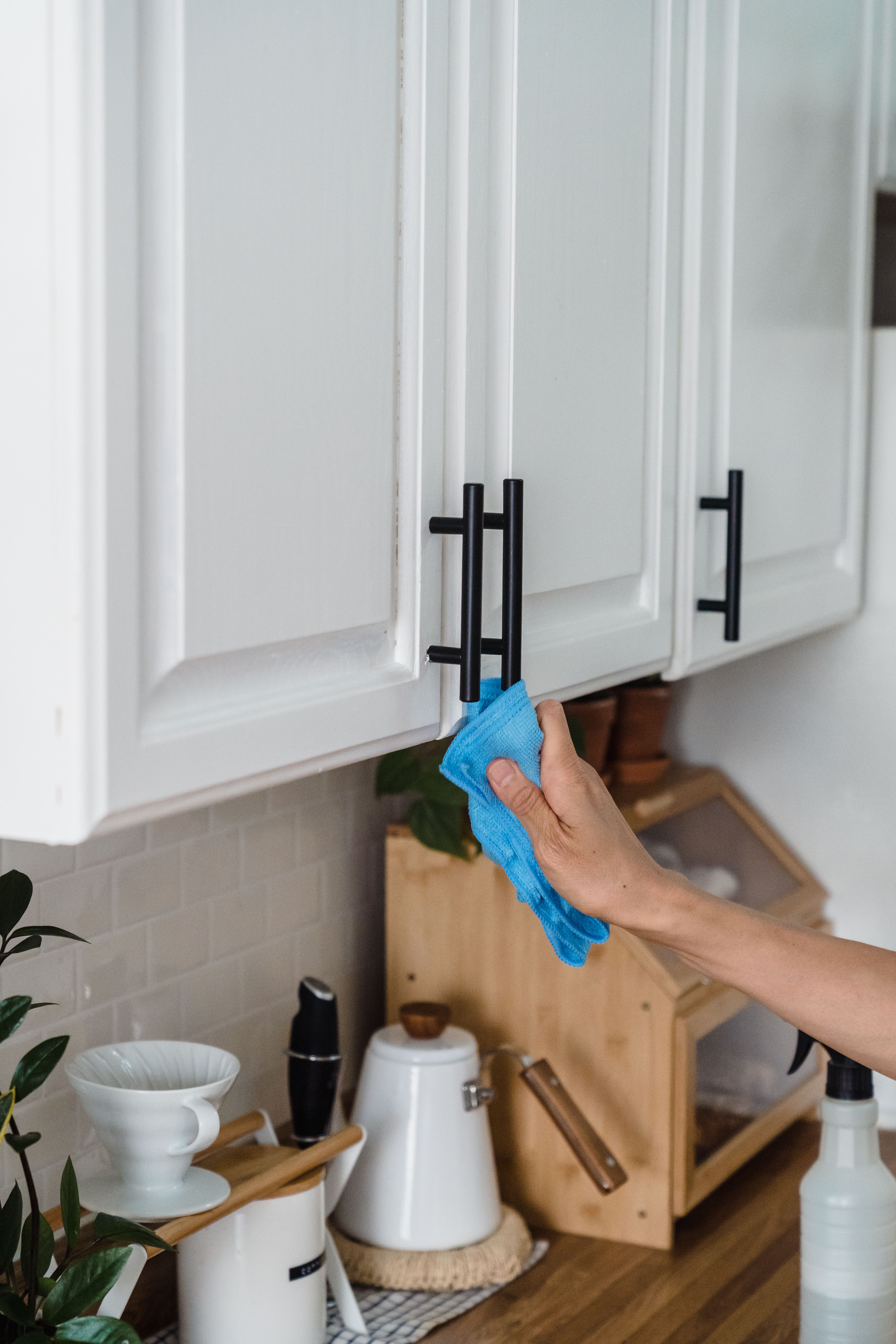 A person cleans a black cabinet handle in a white kitchen. | Source: Pexels