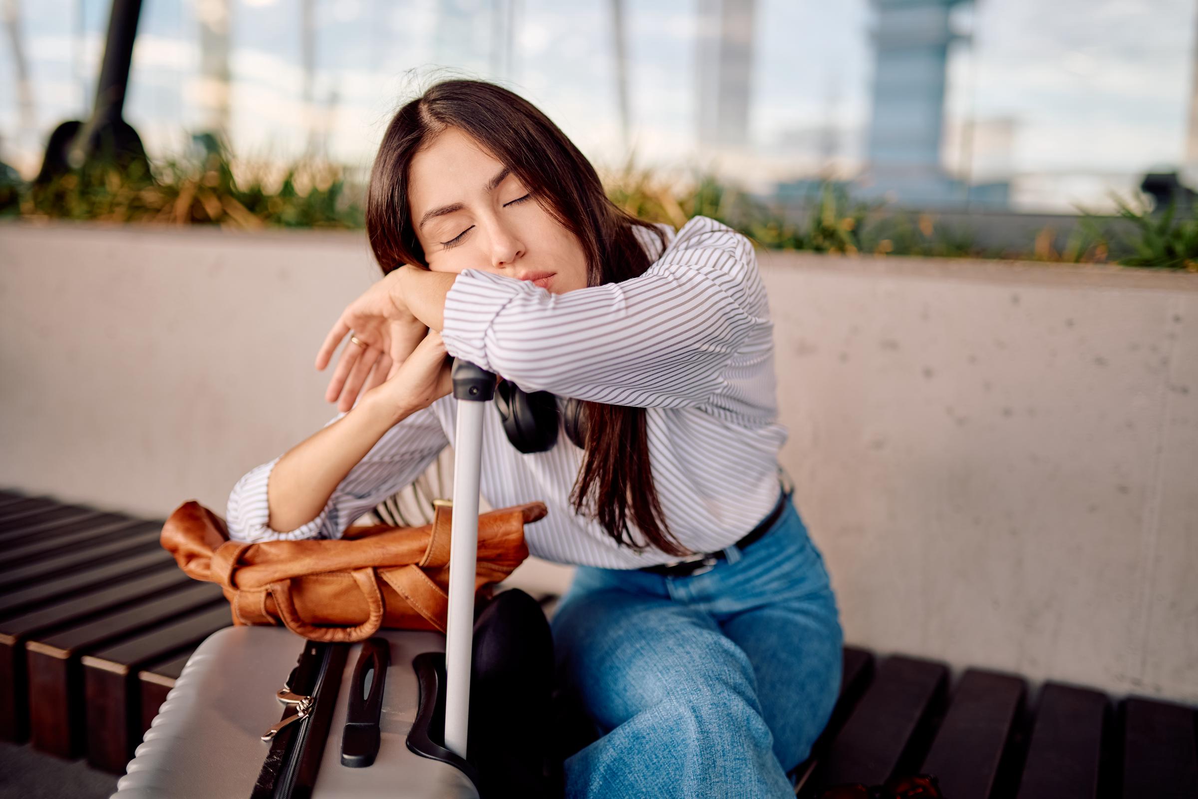 A woman dozing off on her suitcase handle at an airport | Source: Getty Images